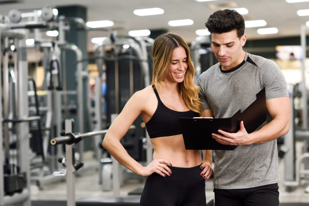 The workout split for muscle growth: Which one is right for you? A fitness trainer and a female athlete reviewing a structured workout plan in a gym environment